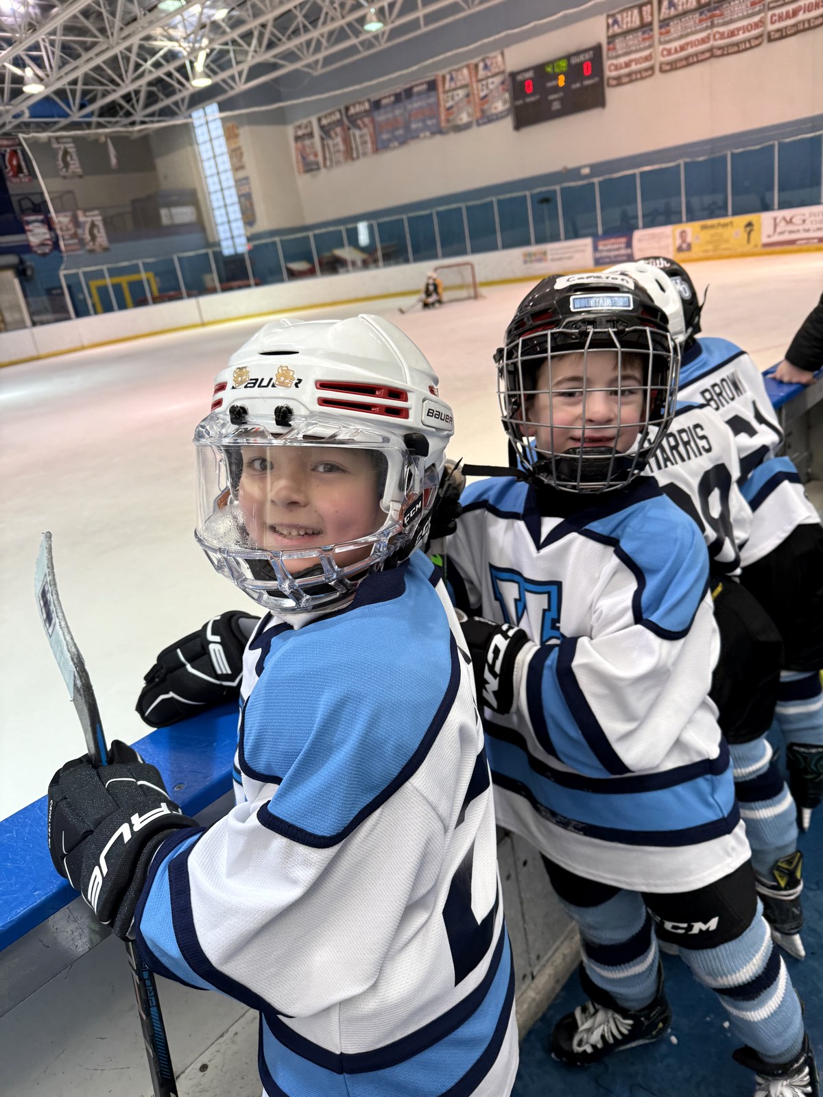 Two smiling MTL Mites players at the boards during a game